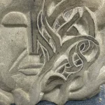 Partly carved dryad, with closed eyes and twining vines. Carved from stone with hand-tools beside it.